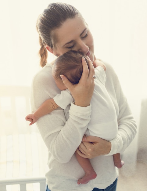 Getinte portret van lachende zorgzame moeder met schattige babyjongen op handen
