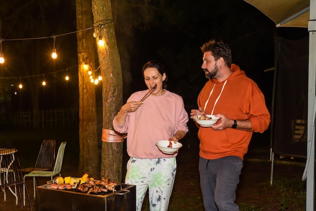 Getrouwd echtpaar man en vrouw eten barbecue worstjes's nachts in de buurt van bliksem kralen in de backya