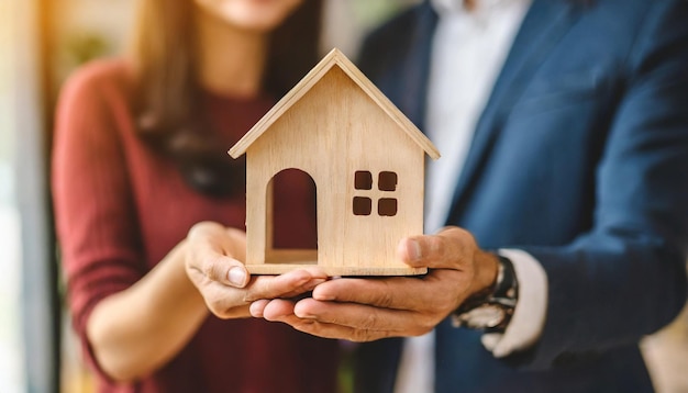 getrouwde paren met handen die een houten huis vasthouden dat het bezit van een huis en de aspiraties van onroerend goed symboliseert