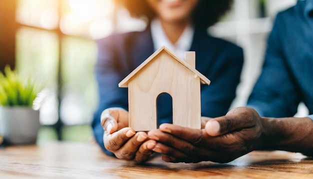 getrouwde paren met handen die een houten huis vasthouden dat het bezit van een huis en de aspiraties van onroerend goed symboliseert