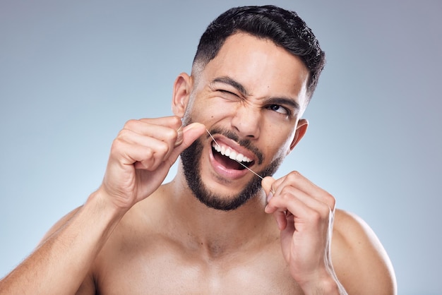 Getting every single morsel out. Shot of a handsome young man flossing his teeth against a studio background.