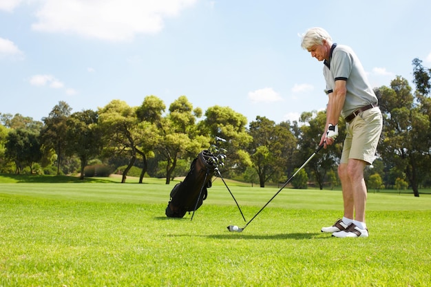 彼のスタンスを正しくするゴルフコースでスイングする準備をしている年配の男性