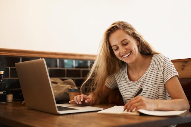 カフェのテーブルで勉強するために彼女のラップトップを使用して幸せな若い学生のそのテストショットをエースする準備をしている