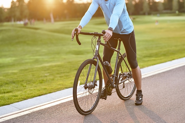 Фото Готовимся к поездке. обрезанный снимок стоящего на шоссейном велосипеде гонщика в спортивной одежде.