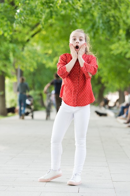 Getting a shocking surprise Surprised small child with adorable stylish look Little girl with long blond hair in stylish wear Stylish kid playing in summer park Her wardrobe is stylish yet casual