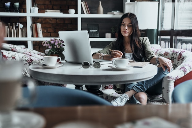 Getting things done. Beautiful young woman holding a pencil and looking at laptop 