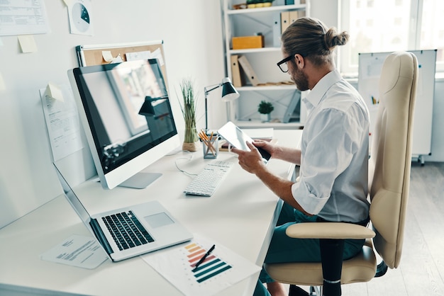 Getting things done. Good looking young man in shirt using digital tablet while sitting in the office