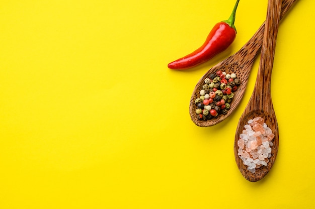 Geurige kruiden in een lepel en rode peper geïsoleerd op gele achtergrond, bovenaanzicht. Biologische vegetarische voeding, kruideniersassortiment, natuurlijke ecoproducten, gezond levensstijlconcept