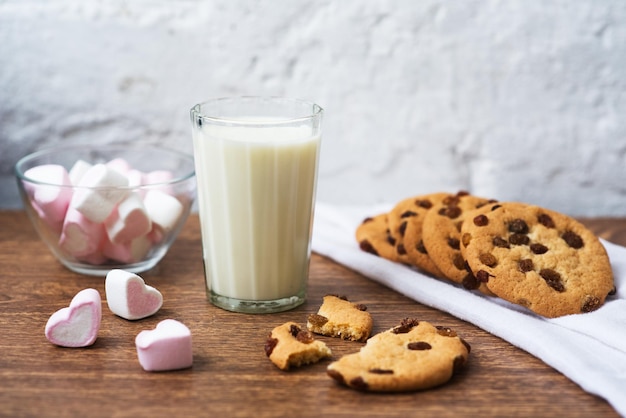 Geurige smakelijke zelfgemaakte koekjes met rozijnen marshmallows in de vorm van harten en glas verse melk op tafel