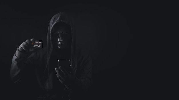 Gevaarlijke anonieme hacker man in hooded gebruik smartphone met creditcard