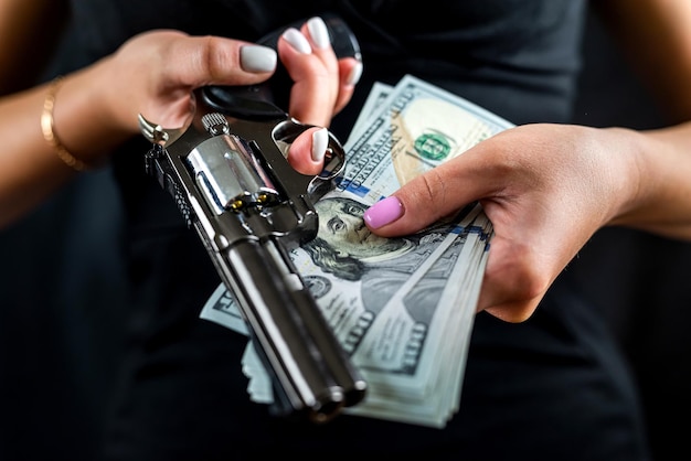 Gevaarlijke vrouw in een zwarte jurk houdt een pistool en geld dollars vast geïsoleerd op een effen achtergrond
