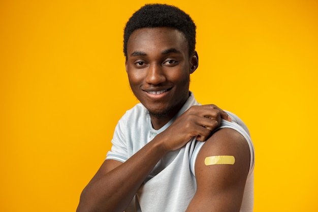 Gevaccineerde afro-amerikaanse man die zijn arm toont tegen gele achtergrond