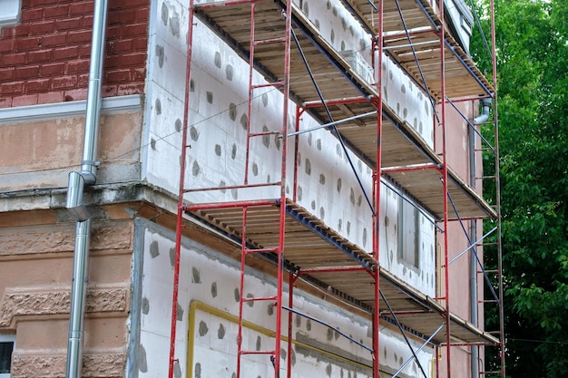 Gevel van het gebouw in renovatiewerken met constructiesteigerframe Muurisolatie met piepschuimplaten voor energiezuinige woning