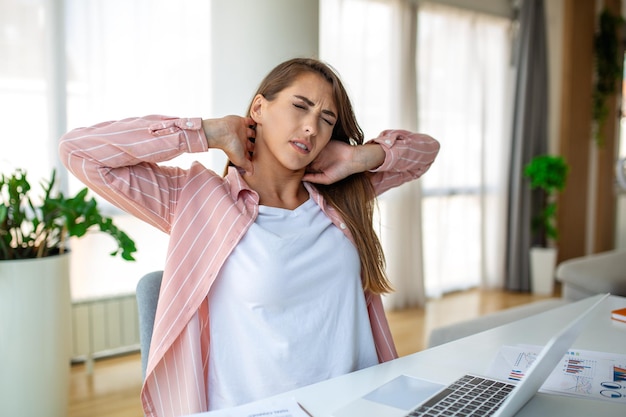 Foto gevoel van uitputting frustreerde vrouw die uitgeput lijkt en haar nek masseert terwijl ze op zijn werkplaats zit