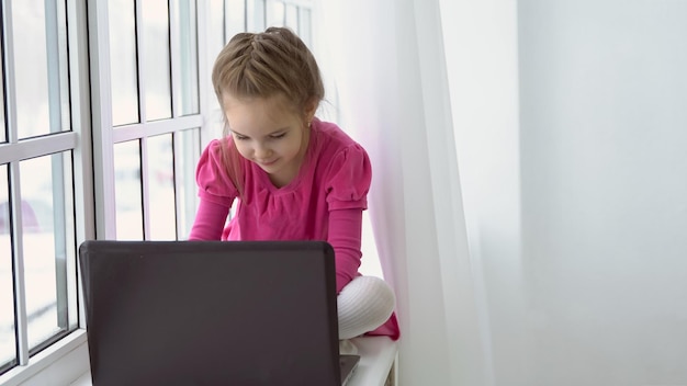 Gevorderd meisje in een roze jurk zit bij het raam met een laptop.