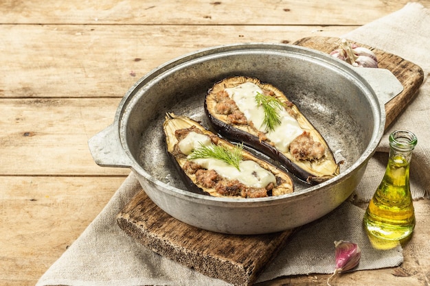 Gevulde aubergine klaar om te eten met gehakt, groenten en kruiden. Houten achtergrond, keukengerei, rustieke stijl, kopieer ruimte