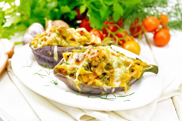 Gevulde aubergine met gerookte borst, tomaten, uien, wortelen met knoflook, kaas en kruiden in een bord op een theedoek op achtergrond van licht houten bord