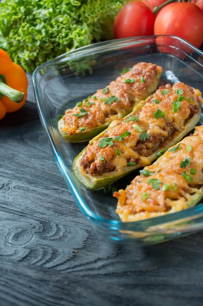 Gevulde courgette met gehakt en geraspte kaas in een glazen bakplaat. Donkere houten achtergrond Gezond evenwichtsvoedsel Koken voedsel.