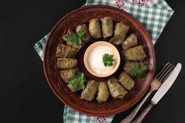 Gevulde druivenbladeren - traditionele mediterrane keuken, dolma op een bruin bord met verse peterselie en knoflooksaus op een zwarte achtergrond, close-up, bovenaanzicht