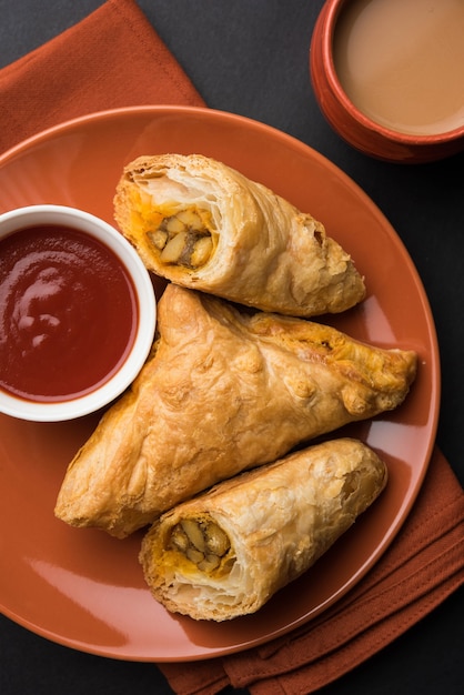 Gevulde groentebladerdeeg of samosa, beroemde Indiase bakkerijsnack, geserveerd met tomatenketchup en hete thee, selectieve focus