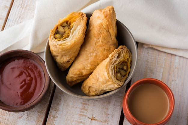 Gevulde groentebladerdeeg of samosa, beroemde Indiase bakkerijsnack, geserveerd met tomatenketchup en hete thee, selectieve focus