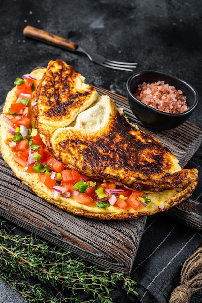 Gevulde omelet met tomaten, rode paprika en ui op een houten bord Zwarte achtergrond Bovenaanzicht