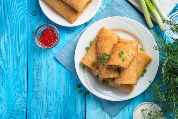 Gevulde pannenkoeken versierd met dille en ui met rode kaviaar, zure room op een blauwe achtergrond. Traditionele gebakken Russische pannenkoeken. Bovenaanzicht, kopieer ruimte.