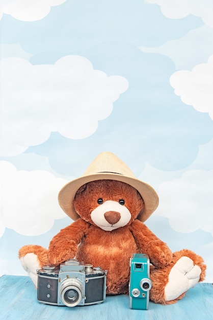 Gevulde stuk speelgoed teddybeer zit dichtbij de oude fotocamera en retro videocamera op een blauwe hemelpastelkleur.