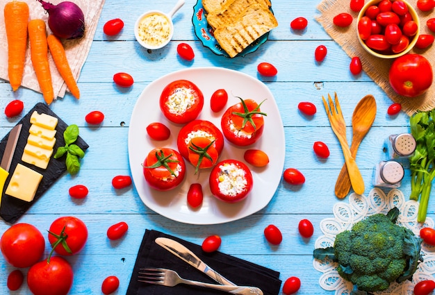 Gevulde tomaten met kaas en verschillende groenten, op een houten tafel,