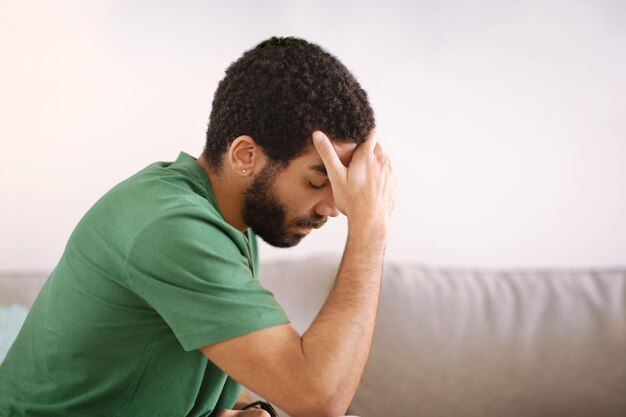 Gewanhoopte, vermoeide, trieste jonge man uit het Midden-Oosten die op de bank zit en lijdt aan stress en hoofdpijn