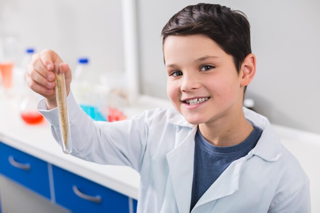 Gewas in vail. Slimme goed uitziende tevreden jongen flesje houden terwijl staren naar de camera en dressing in laboratoriumjas