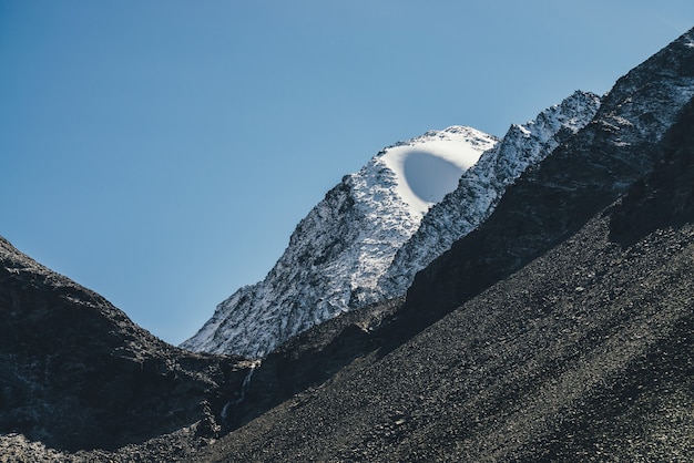 Geweldig berglandschap met witte sneeuw op zwarte rotsen in blauwe lucht. sfeervol alpenlandschap met sneeuwbol op de bergtop in de zon. mooie ongebruikelijke bolvormige sneeuwpiek in zonlicht.