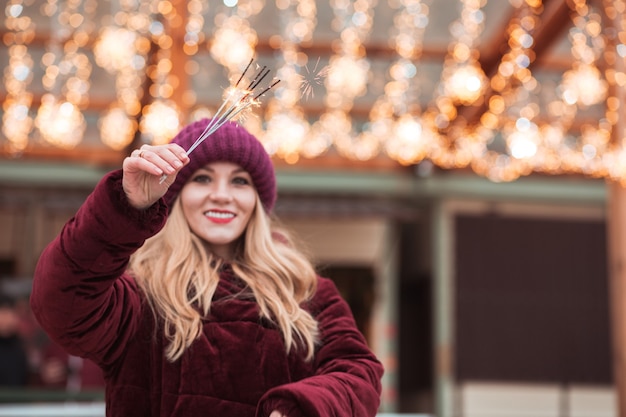 Geweldig blond meisje met gloeiende Bengaalse lichten op de kerstmarkt in Kiev. Vervagingseffect