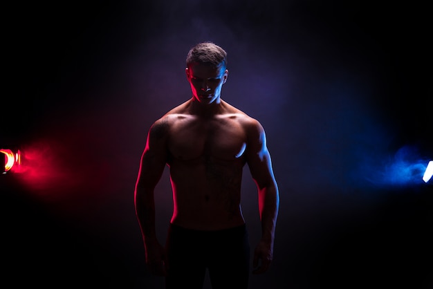 Geweldig bodybuilder silhouet. Knappe macht atletische man bodybuilder. Fitness gespierd lichaam op donkere kleur rook scène. Perfecte reu. tattoo, poseren.