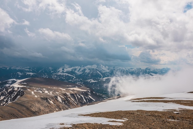 Geweldig bovenaanzicht door wolken naar hoge besneeuwde bergen schilderachtig landschap met prachtige sneeuwbergen in lage wolken sfeervol alpenzicht van stenen heuvel naar sneeuwgebergte met lage wolken