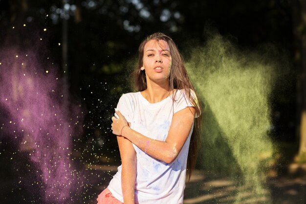 Geweldig gebruind Aziatisch model gekleed in een wit overhemd, spelend met groene en paarse Holi-verf