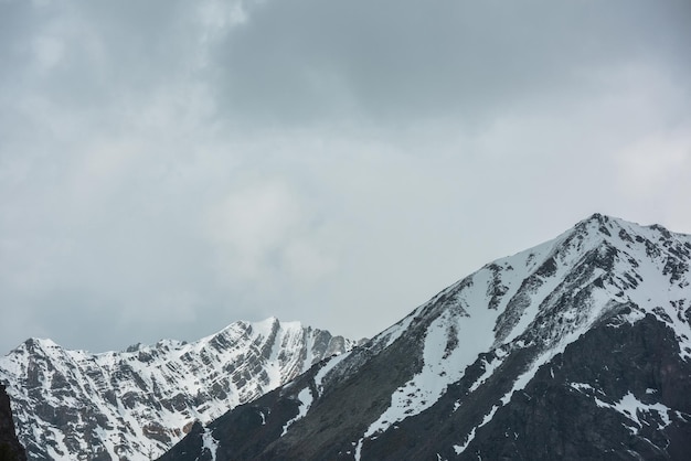 Geweldig landschap met hoge besneeuwde bergketen met scherpe rotsen in zonlicht in bewolkte lucht Dramatisch uitzicht op sneeuwbergen bij wisselvallig weer Sfeervol landschap met witte sneeuw op zwarte rotsen