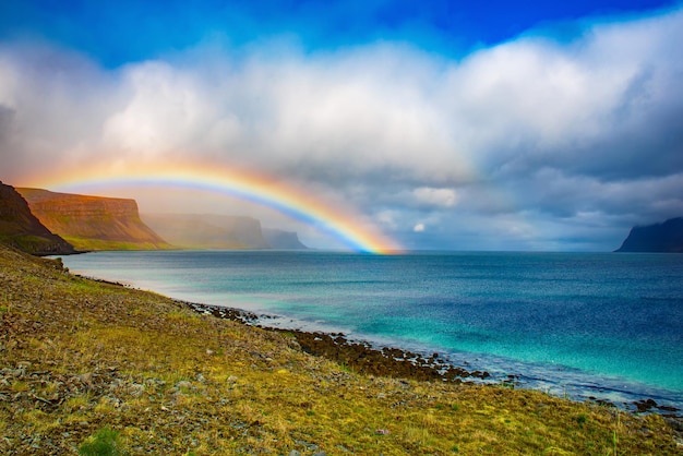 Geweldig zomerlandschap met blauwe zee, witte wolken en regenboog. IJsland, Europa