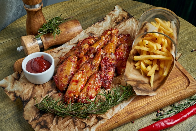 Geweldige biersnack - pittig gebakken buffelvleugels. bbq-vleugels met garnituur van frietjes op een houten dienblad. bovenaanzicht, plat eten. pub eten