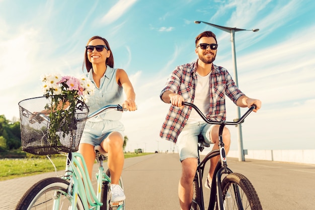 Geweldige dag om te fietsen. Lage hoekmening van vrolijk jong koppel glimlachend en rijdend op fietsen