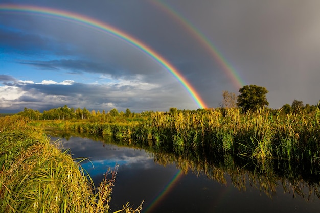 Geweldige dubbele regenboog boven de kleine landelijke rivier