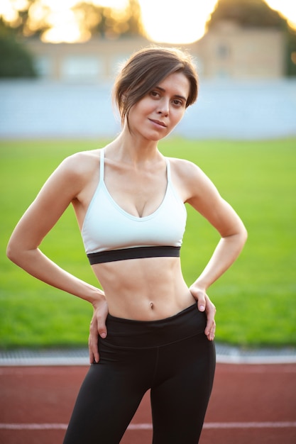 Geweldige fitnessvrouw draagt sportkleding met een atletisch lichaam poserend in het stadion bij zonsondergang