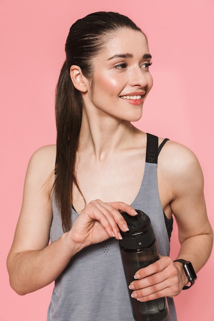 geweldige mooie jonge mooie fitness vrouw met fles met water drinken geïsoleerd over roze muur