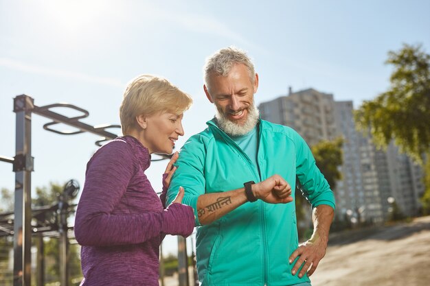 Geweldige resultaten gelukkig volwassen familiepaar in sportkleding kijken naar smartwatch en training controleren