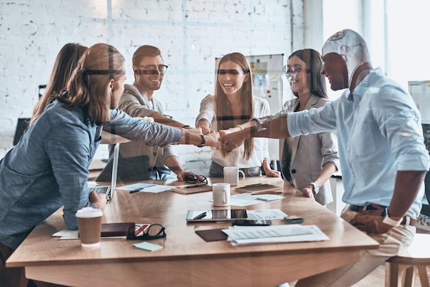 Geweldige resultaten. Groep zakencollega's die vuisten bij elkaar houden in een symbool van eenheid terwijl ze achter de glazen wand in de bestuurskamer werken