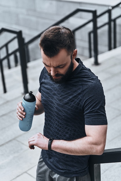 Geweldige resultaten. Knappe jongeman in sportkleding die naar zijn fitnesstracker kijkt