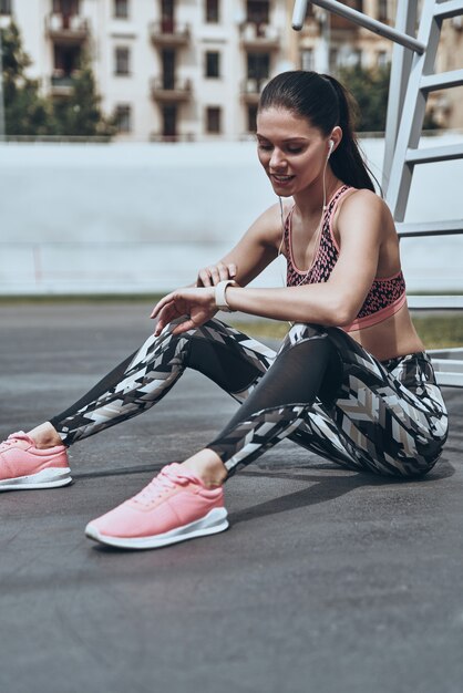 Geweldige resultaten. Mooie jonge vrouw in sportkleding die de tijd controleert terwijl ze buiten zit