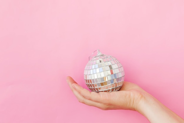 Gewoon minimaal ontwerp vrouwelijke vrouw hand met kerst ornament disco bal geïsoleerd op roze plakken...