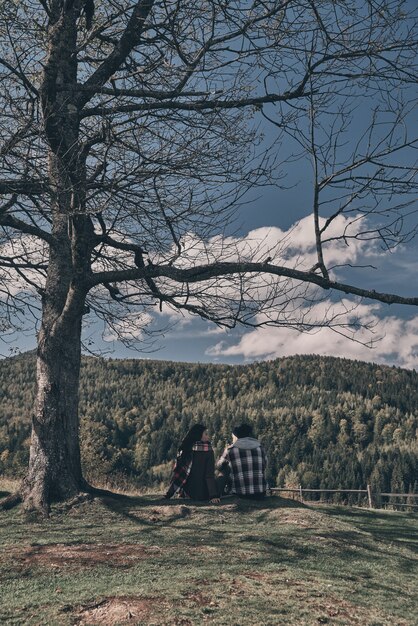 Gewoon ontspannen en diep ademhalen. Achteraanzicht van een jong stel dat het uitzicht bewondert terwijl ze op de bergtop onder de boom zitten