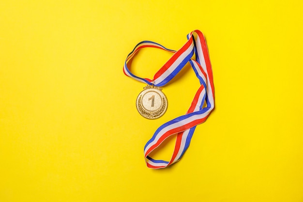 Gewoon plat leggen ontwerp winnaar of kampioen gouden trofee medaille geïsoleerd op gele kleurrijke achtergrond. Overwinning eerste plaats van de competitie. Winnen of succes concept. Bovenaanzicht kopie ruimte.